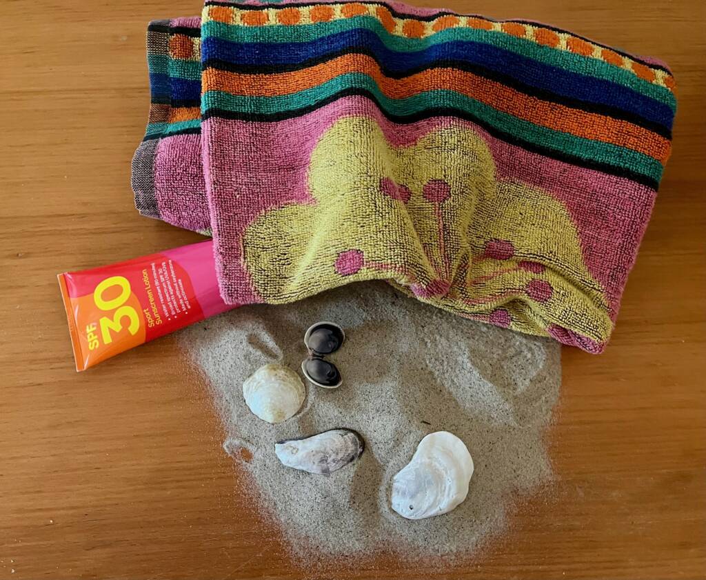 Beach items that include sunscreen, towel, sand, and shells.
