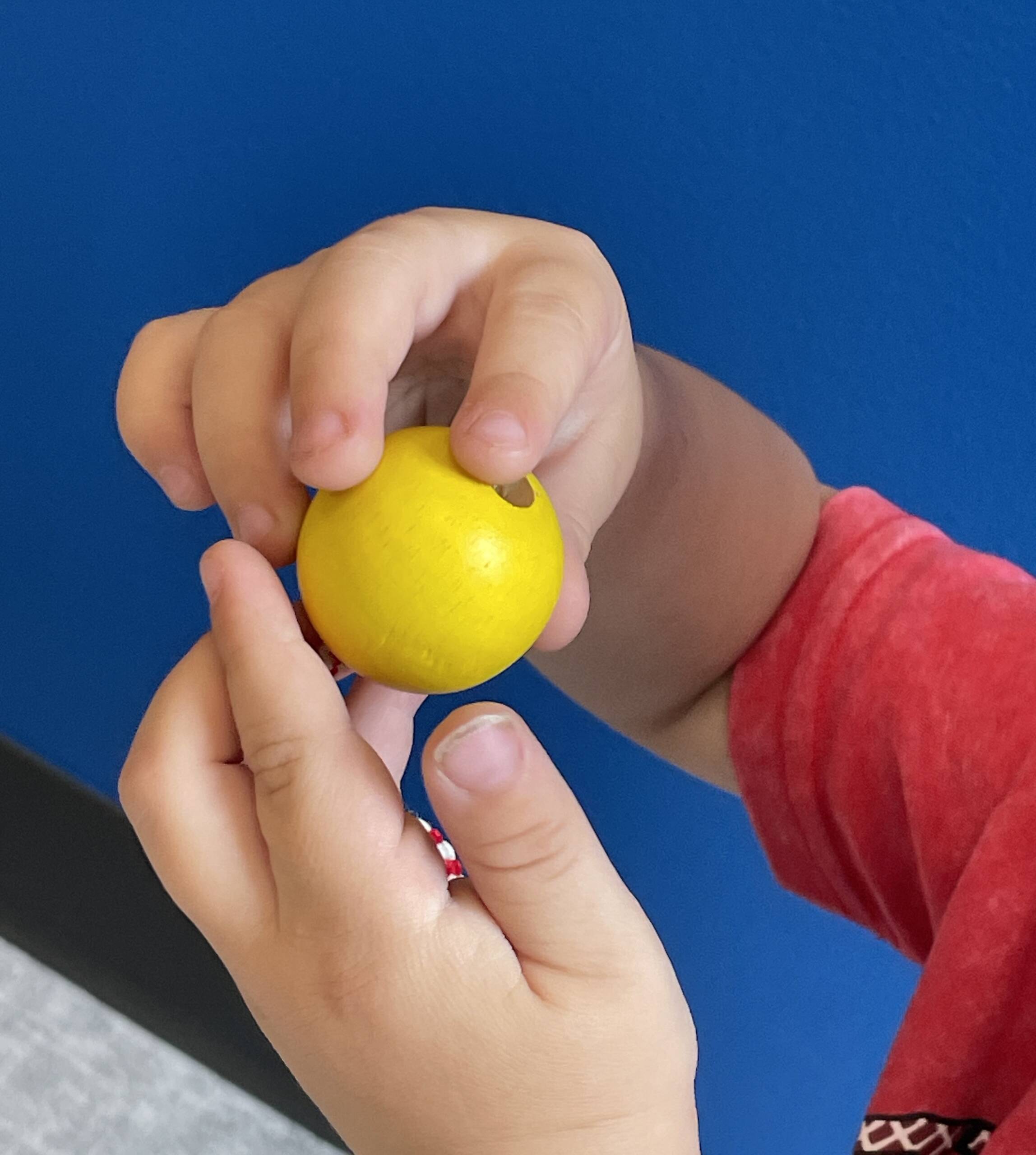 A child's hands exploring a wooden bead with a drilled hole in the middle.