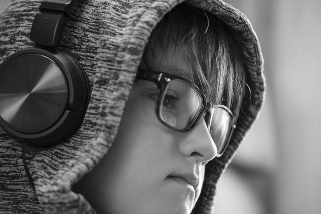 Child with a glasses and a hooded sweatshirt on listening with headphones.