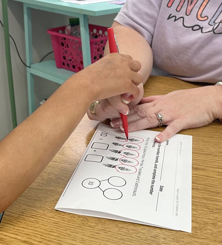 Student circling items on a worksheet with a marker and help from an adult. 