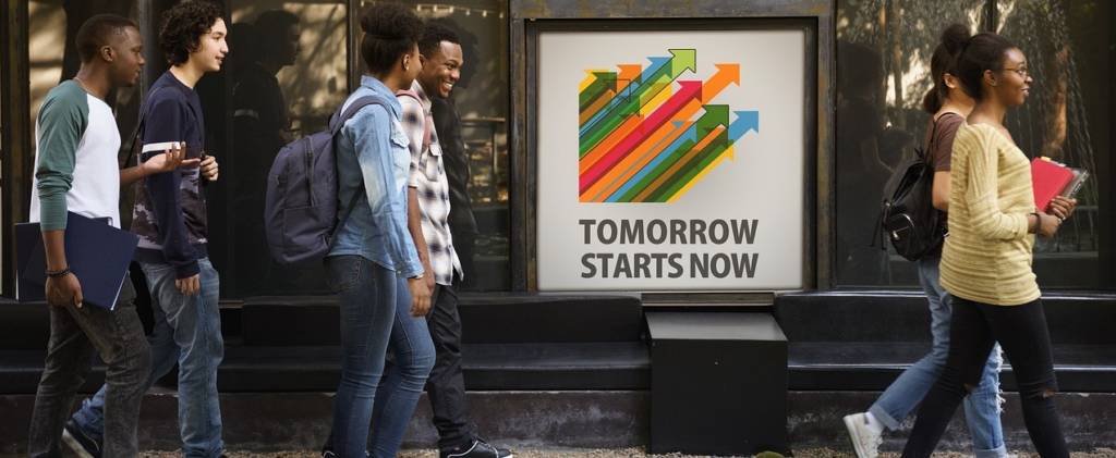 College students walking with books in their hands and backpacks and a sign that says, "tomorrow starts now".