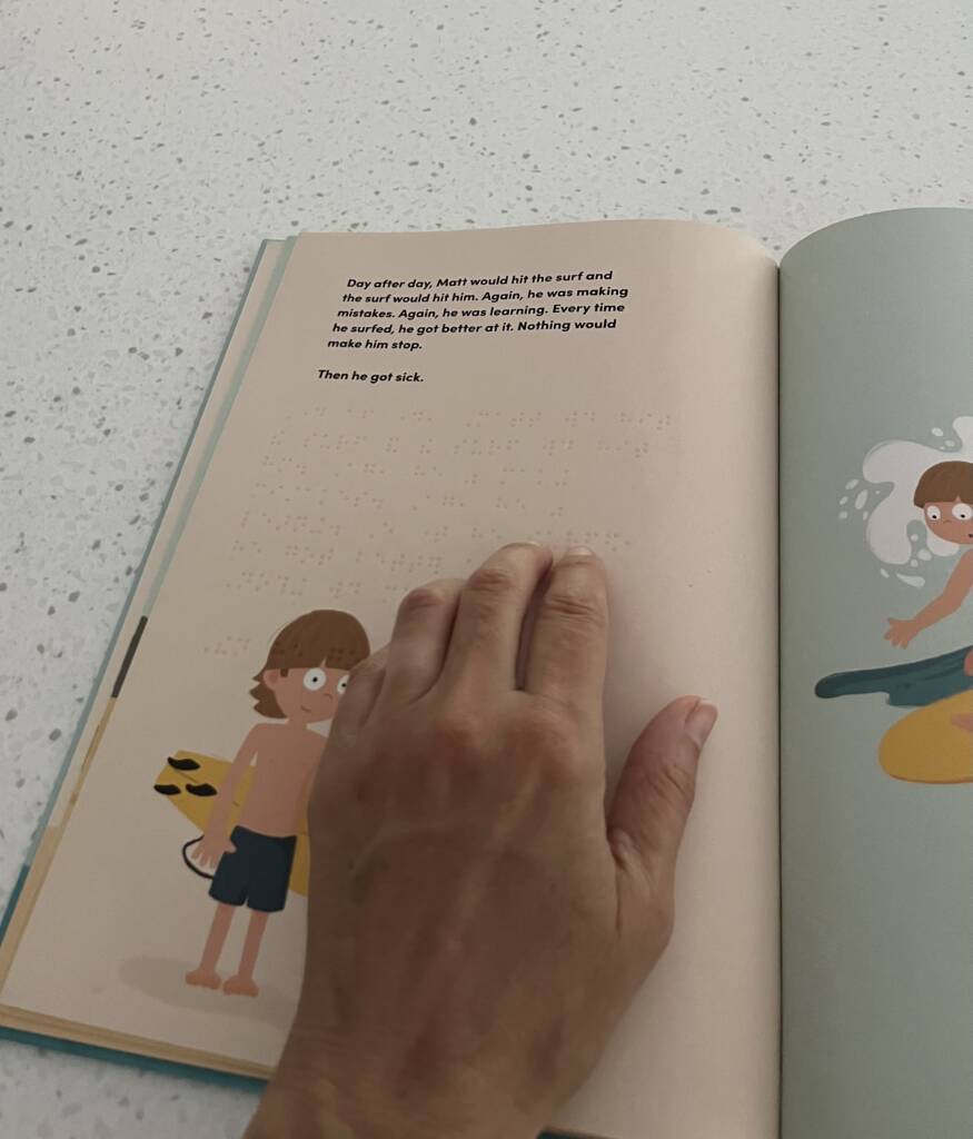 Hand touching the braille on the page of the book: Surfing in the Dark.