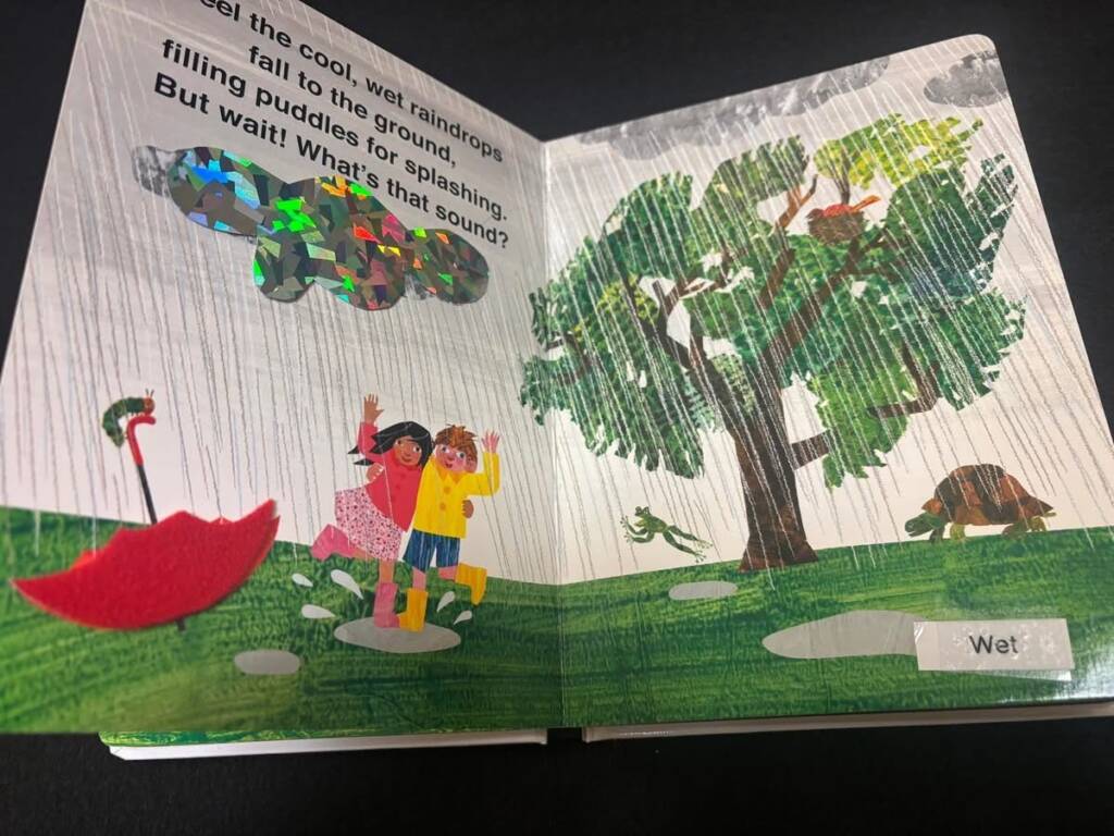 A page in the books that has been adapted with a felt umbrella and a glossy textured rain cloud. 