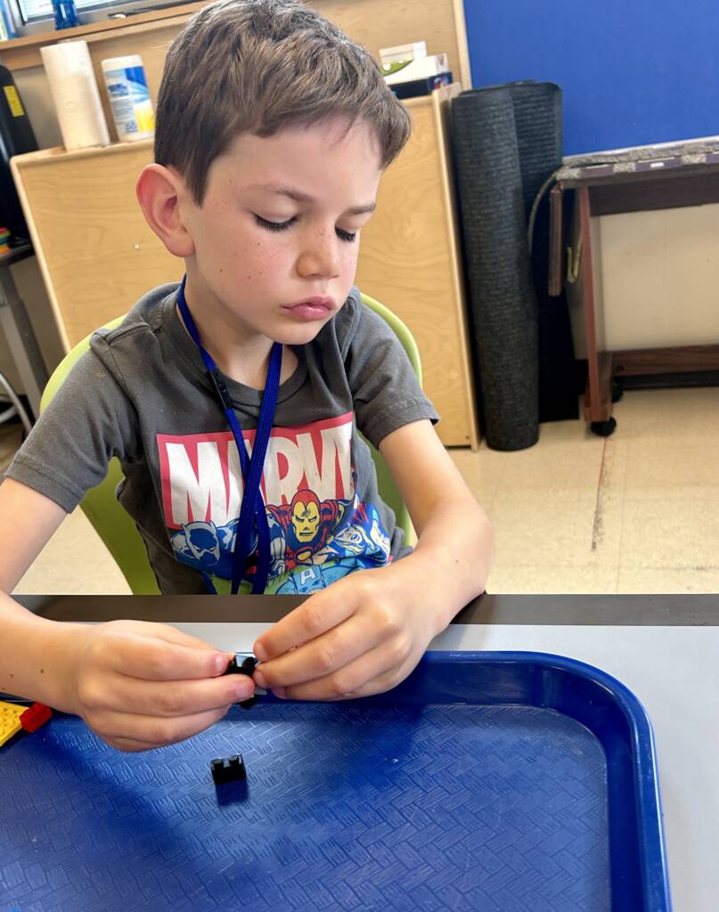 Boy sitting with a tray touching a lego piece.