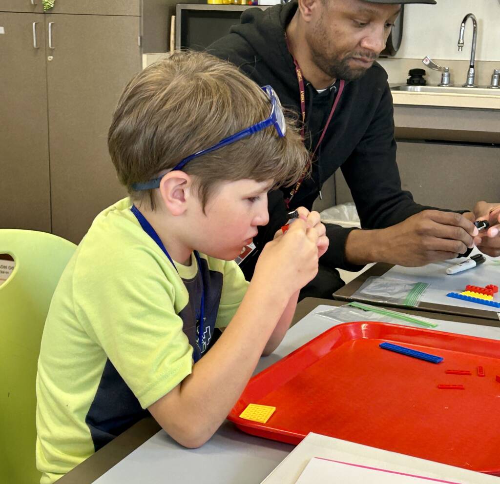A boy exploring legos with a teacher next to him also using legos.