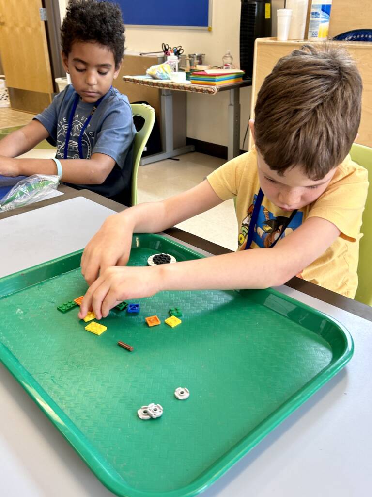 Two boys at a table exploring legos on individual trays. 