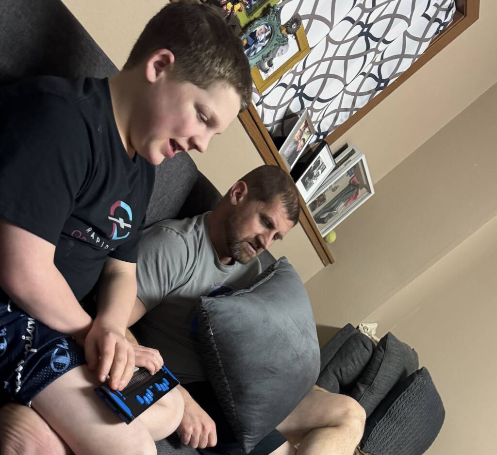 Liam with an adult using his refreshable braille at home on the sofa