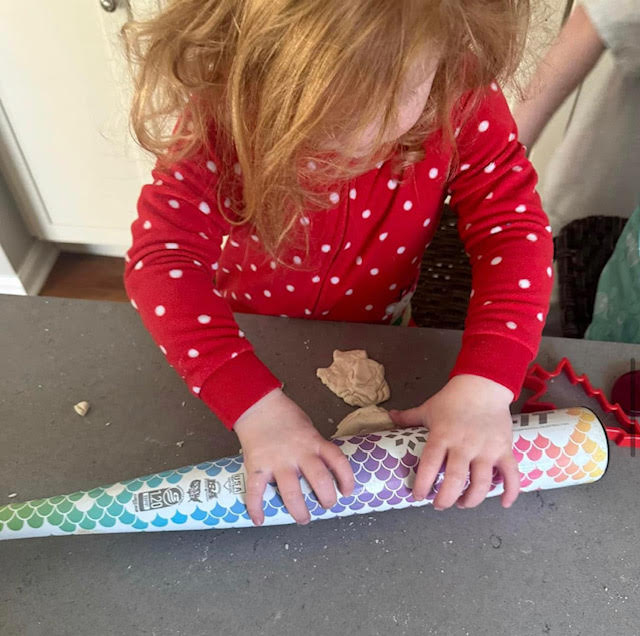 Young child rolling out a ball of salt dough with a colorful baseball bat