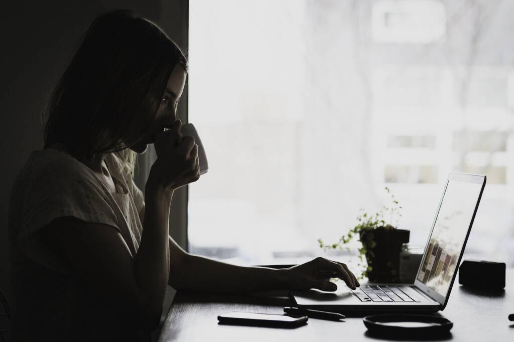 Young woman sitting and looking at her laptop while sipping tea.